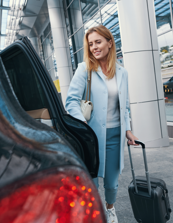 Woman entering car with suitcase at airport.